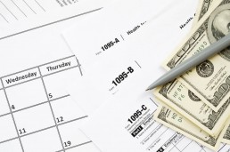 three 1095 reporting forms with a stack of cash, pen and calendar