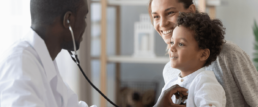 pediatrician listening to patient's heart with stethoscope while mom watches